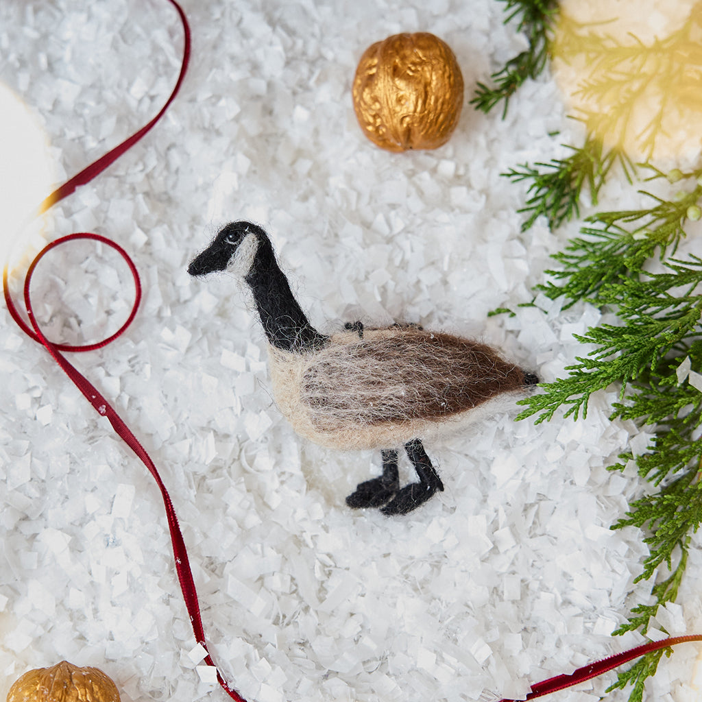 Craftspring’s Canada Goose Ornament — needle felted with soft wings and beaded eyes — displayed on snowy ground with golden walnuts, a festive holiday scene full of warmth, heirloom beauty, and Christmas gifting cheer, ethically crafted by artisans using sustainable wool.