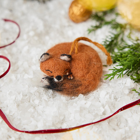 Craftspring’s Sleepy Fox Ornament — needle felted, curled up with a cute face, fluffy tail, and whiskers — displayed on snow among evergreens, evoking cozy holiday magic, woodland charm, and the joy of Christmas gifting, ethically crafted by artisans using sustainable wool.