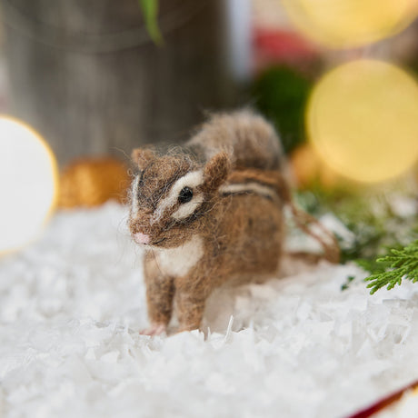 Handmade felt Fuzzy Chipmunk ornament from Craftspring displayed in the snow with evergreens — needle-felted with stripes along its back and a cute face, ethically crafted by artisans using sustainable wool for heirloom-quality Christmas gifting and decor.