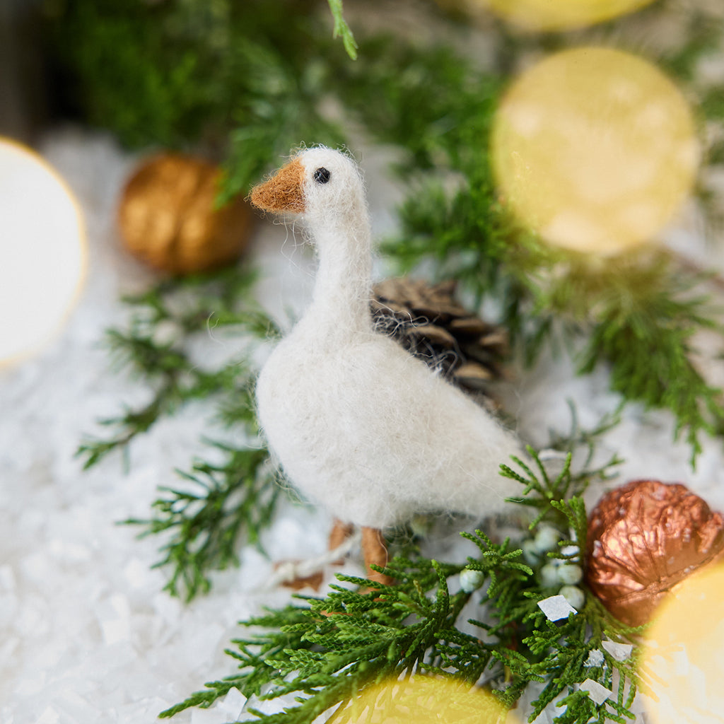 Craftspring’s Goose Ornament — needle felted with fluffy feathers and beaded eyes — displayed on snow with evergreens and golden walnuts, a festive holiday scene full of heirloom beauty, warmth, and Christmas gifting cheer, ethically crafted by artisans using sustainable wool.