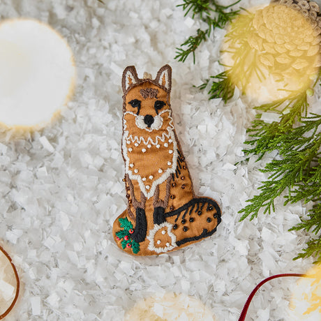 Craftspring’s handmade satin Fox Beaded Ornament — featuring intricate beaded and embroidered details, displayed on snow with evergreens and a red ribbon for a festive holiday scene, perfect for Christmas decorating or gifting, ethically crafted by artisans using sustainable materials.