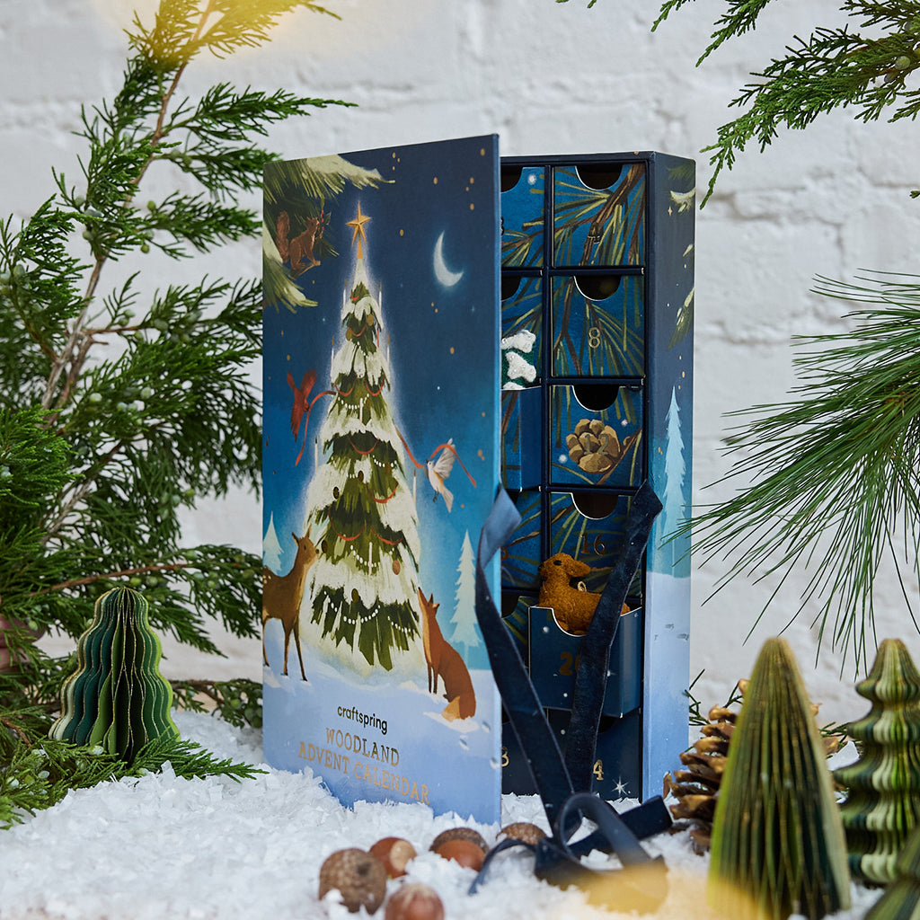 Craftspring’s Woodland Minis Advent Calendar — shown opening with velvet ribbon ties, a glimpse of the drawers inside, and one drawer open with a mini deer ornament peeking out, creating a charming, gift-filled holiday scene, ethically crafted by artisans using sustainable wool.