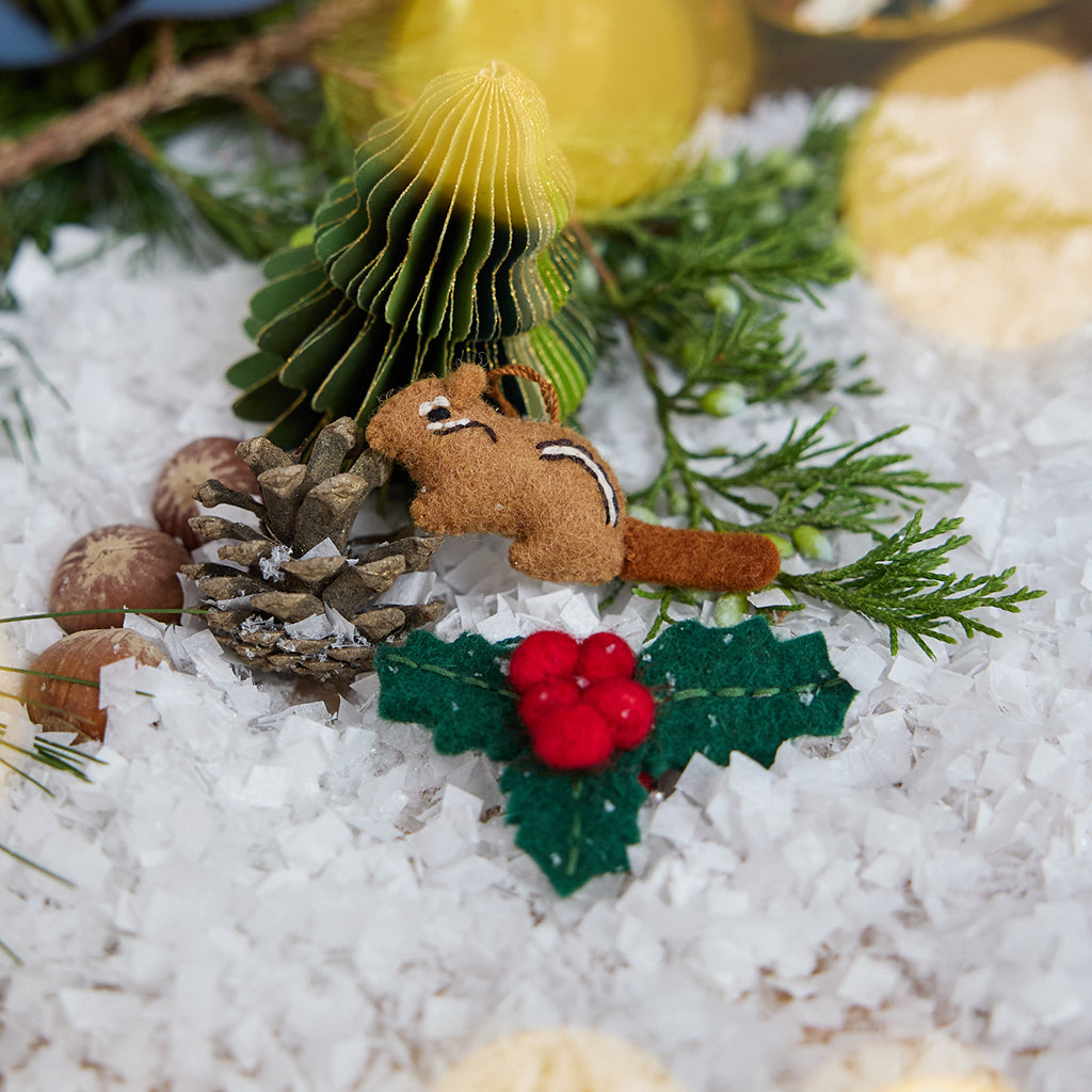 Craftspring’s handmade Woodland Minis Advent Calendar — close-up of two mini ornaments, a chipmunk and holly, displayed among evergreens and snow, highlighting the intricate woodland Christmas details, ethically crafted by artisans using sustainable wool.