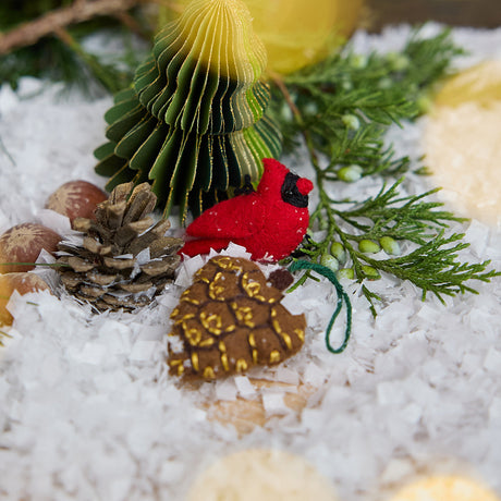 Craftspring’s handmade Woodland Minis Advent Calendar — close-up of two mini ornaments, a cardinal and a pinecone, displayed among evergreens and snow, highlighting the intricate woodland Christmas details, ethically crafted by artisans using sustainable wool.