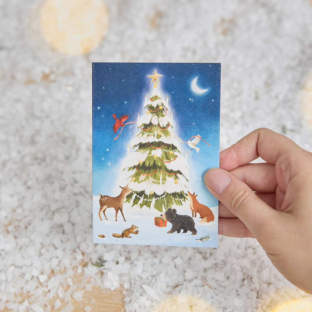 Craftspring’s Woodland Tree Greeting Card — held in hand over snow, featuring woodland animals around a glowing winter Christmas tree, ethically printed in the USA on natural textured paper, perfect for sharing holiday cheer and gifting.
