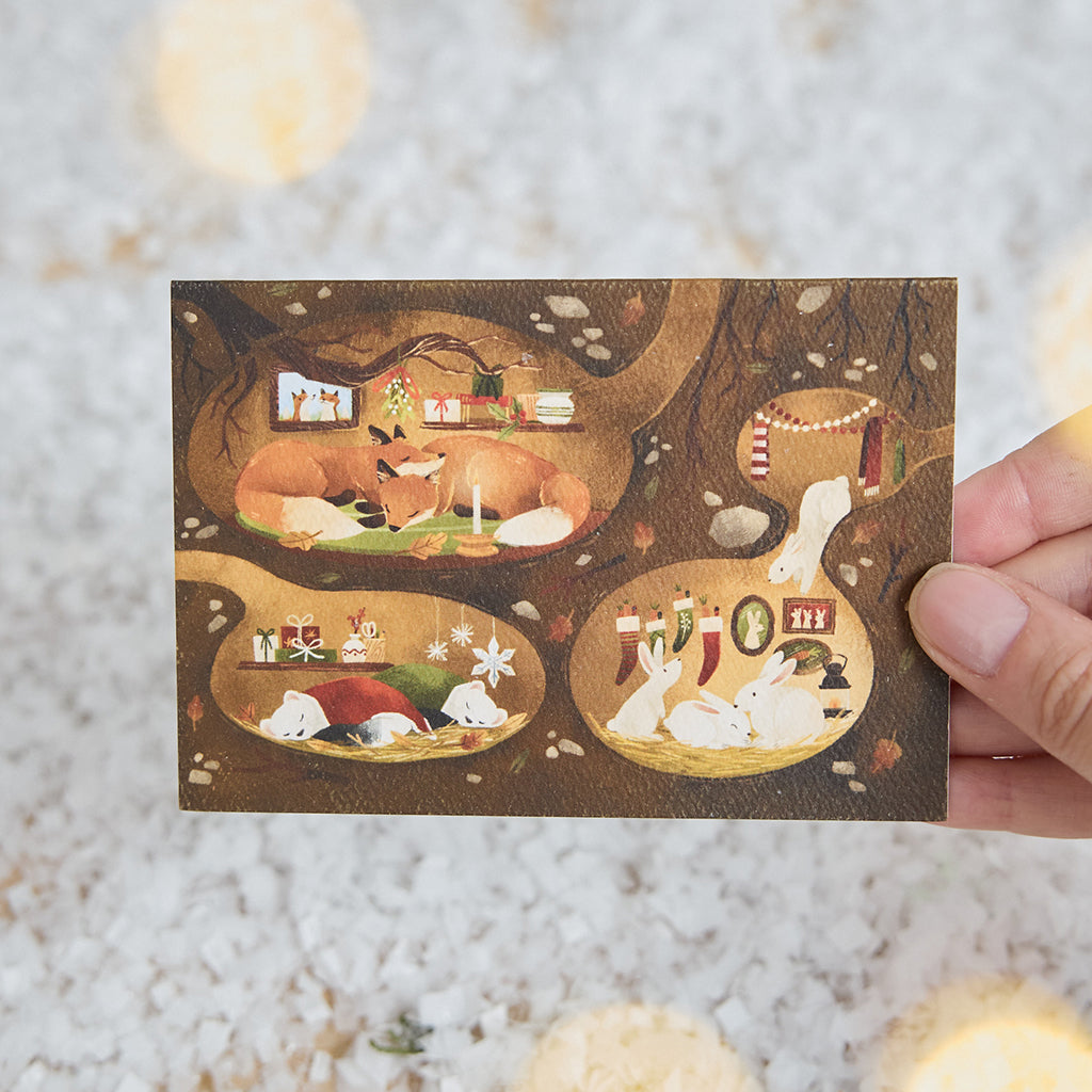 Craftspring’s Woodland Burrows Greeting Card — held in hand over snow, featuring woodland animals nestled in cozy holiday burrows, ethically printed in the USA on natural textured paper, perfect for sharing holiday cheer and gifting.