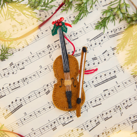 Cello Ornament displayed on sheet music with evergreens — handmade felt holiday decor with beaded and embroidered details, ethically crafted by artisans using sustainable wool.
