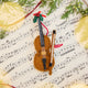 Cello Ornament displayed on sheet music with evergreens — handmade felt holiday decor with beaded and embroidered details, ethically crafted by artisans using sustainable wool.