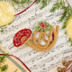 Craftspring’s French Horn Ornament displayed on sheet music with fresh evergreens — handmade felt holiday decor with intricate golden embroidery, beading, and mistletoe, ethically crafted by artisans using sustainable wool.