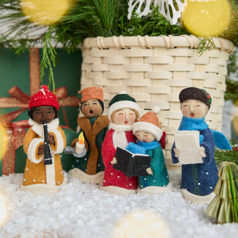Handmade felt Carolers Set of 5 ornaments from Craftspring, featuring four singers and one clarinet player dressed in vintage clothes, with applique and embroidered snow at their feet — sweet-faced holiday decor that can stand on a mantle or hang on a Christmas tree, ethically crafted by artisans using sustainable wool.