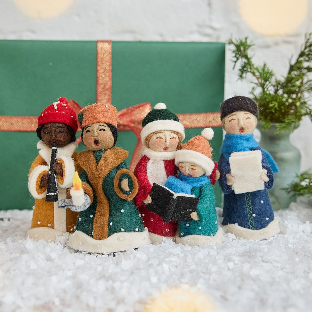 Handmade felt Carolers Set of 5 ornaments from Craftspring, featuring four singers and one clarinet player dressed in vintage clothes, with applique and embroidered snow at their feet — sweet-faced holiday decor that can stand on a mantle or hang on a Christmas tree, ethically crafted by artisans using sustainable wool.