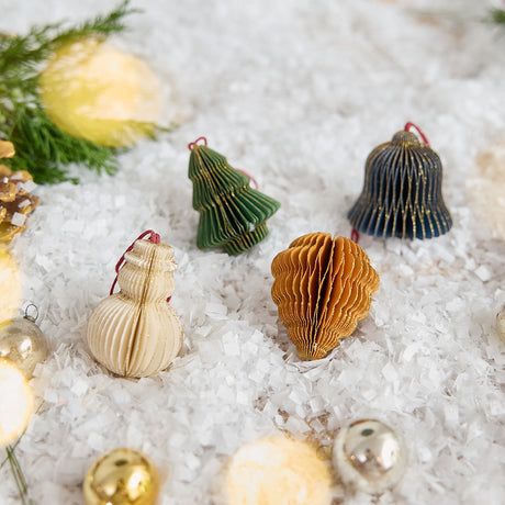 Craftspring’s Classic Christmas Honeycomb Paper Mini Ornaments — Set of 4, displayed on snow with Christmas bobbles and evergreens, showcasing the snowman, bell, pinecone, and tree with gold sparkly edges — handmade by artisans from recycled cotton waste for a festive holiday scene.