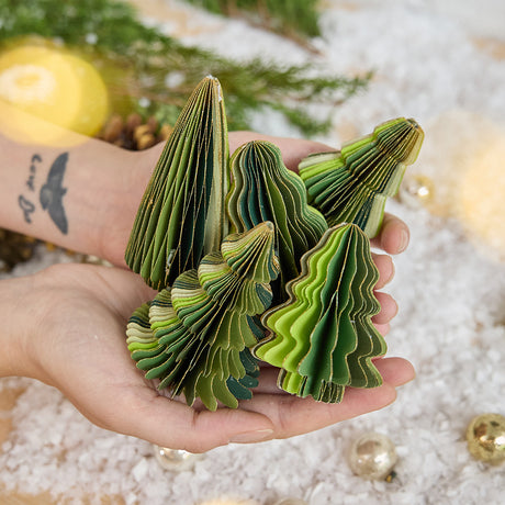 Craftspring’s Green Honeycomb Paper Mini Trees — Set of 5, held in hand over snow, showing their varying shapes, shades of green, and gold-edged details — handmade by artisans from recycled cotton waste, adding festive holiday charm.