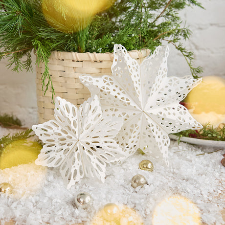 Craftspring’s Paper Snowflakes Christmas Ornaments — Set of 2, large white snowflakes with intricate cutout patterns, one slightly larger than the other — displayed on snow in front of a basket of evergreens, creating a festive holiday scene, ethically handmade by artisans from recycled cotton waste.