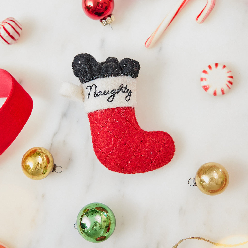 Craftspring’s Naughty Stocking with Coal Ornament — felt red stocking filled with felt coal and beads, embroidered “naughty” — styled among holiday baubles and candy canes, evoking playful holiday cheer, festive warmth, and heirloom-quality Christmas gifting, ethically crafted by artisans using sustainable wool.