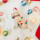 Craftspring’s Yellow Lab in Christmas Lights Ornament — felt dog wrapped in Christmas lights and wearing a Santa hat — styled among holiday baubles and candy canes, evoking festive warmth, playful holiday charm, and heirloom-quality gifting, ethically crafted by artisans using sustainable wool.