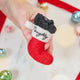 Craftspring’s Naughty Stocking with Coal Ornament — felt red stocking filled with felt coal and beads, embroidered “naughty” — held in hand over holiday baubles, capturing whimsical charm, festive warmth, and heirloom-quality Christmas gifting, ethically crafted by artisans using sustainable wool.