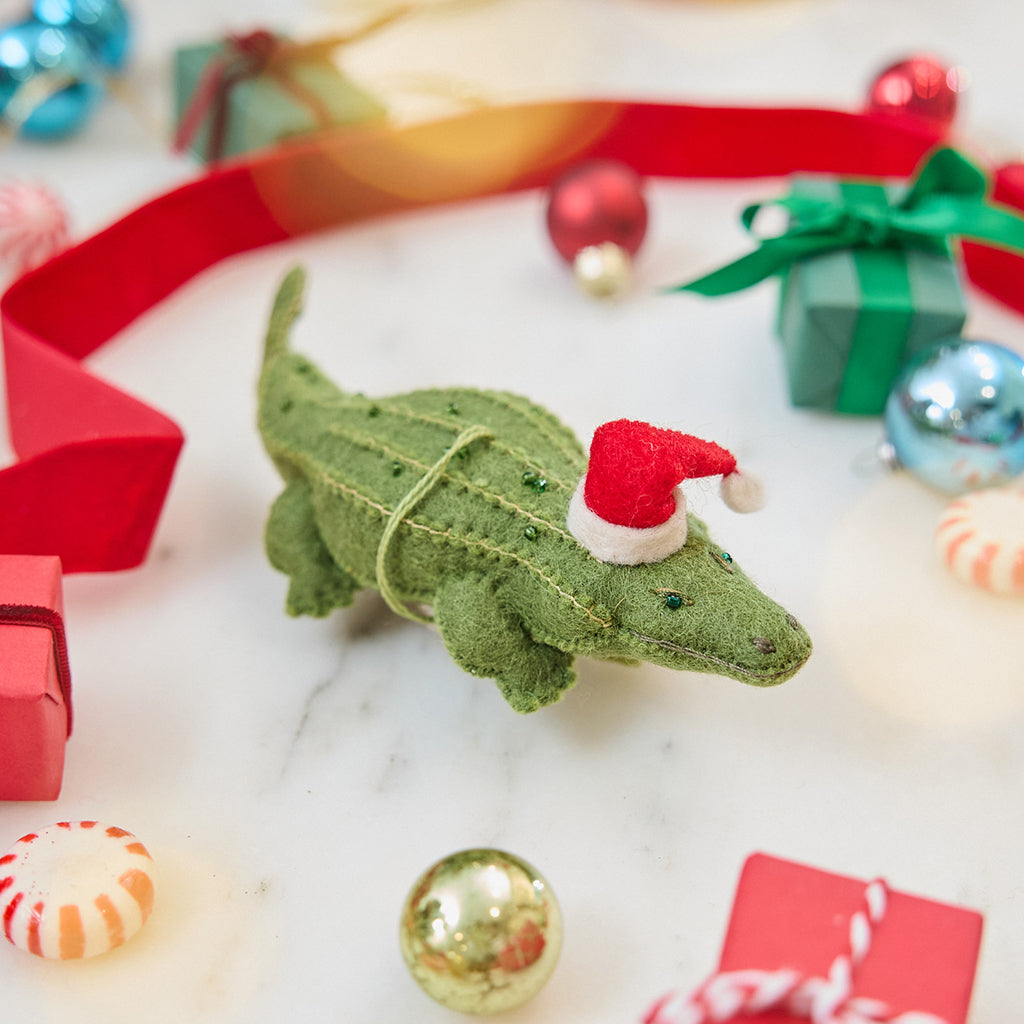 Craftspring’s Santa Alligator Ornament — felt alligator with a beautiful face and embroidered and beaded back ridges — styled among mini presents and baubles, evoking festive warmth, playful holiday charm, and heirloom-quality Christmas gifting, ethically crafted by artisans using sustainable wool.