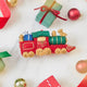 Craftspring’s Toy Train Ornament — felt red and green train with gold embroidery, carrying presents and a teddy bear — styled among holiday baubles and mini presents, evoking festive warmth, playful Christmas cheer, and heirloom-quality charm, ethically crafted by artisans using sustainable wool.