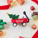Craftspring’s Little Red Wagon with Tree Ornament — felt little red wagon carrying a Christmas tree and garland, with embroidered and beaded details — styled among holiday baubles and mini presents, evoking festive warmth, playful Christmas cheer, and heirloom-quality gifting, ethically crafted by artisans using sustainable wool.