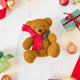 Craftspring’s Holiday Teddy Bear Ornament — felt vintage-style teddy bear wearing a red scarf with holly — styled among holiday baubles and mini presents, evoking festive warmth, playful Christmas cheer, and heirloom-quality gifting, ethically crafted by artisans using sustainable wool.