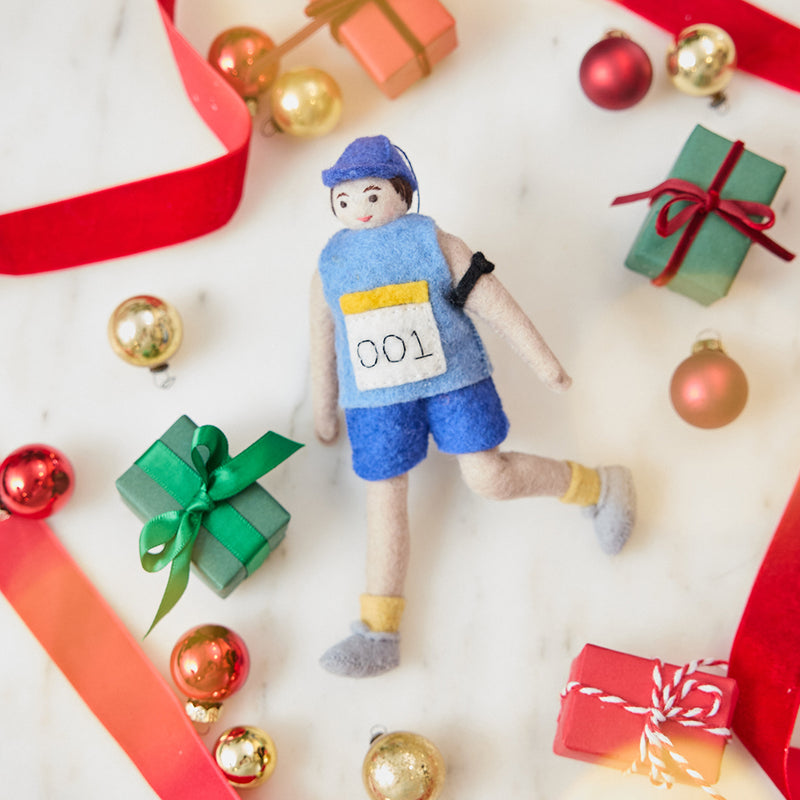 Craftspring’s handmade felt Marathon Runner ornament — featuring a runner with a race bib numbered 001 and an armband, displayed with Christmas baubles, mini presents, and a red ribbon for a festive holiday scene, perfect for Christmas decorating or gifting, ethically crafted by artisans using sustainable wool.
