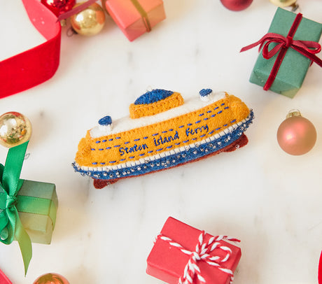 Craftspring’s handmade felt Staten Island Ferry ornament — featuring intricate embroidered details and beaded waves on the iconic orange ferry, displayed with Christmas baubles, mini presents, and a red ribbon for a festive holiday scene, perfect for Christmas decorating or gifting, ethically crafted by artisans using sustainable wool.