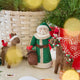 Craftspring’s Emerald Santa Mini Tree Topper, Santa Deer with Bird Friend Ornament, and Forest Grace Rudolph Ornament — felt Santa in a green cloak with beaded details holding a sack of presents with a bird on his shoulder, felt deer with a bird friend, and felt reindeer with delicate holiday details — displayed together in front of a basket of evergreens, evoking cozy holiday warmth, whimsical woodland charm, and heirloom-quality Christmas gifting, ethically crafted by artisans using sustainable wool.