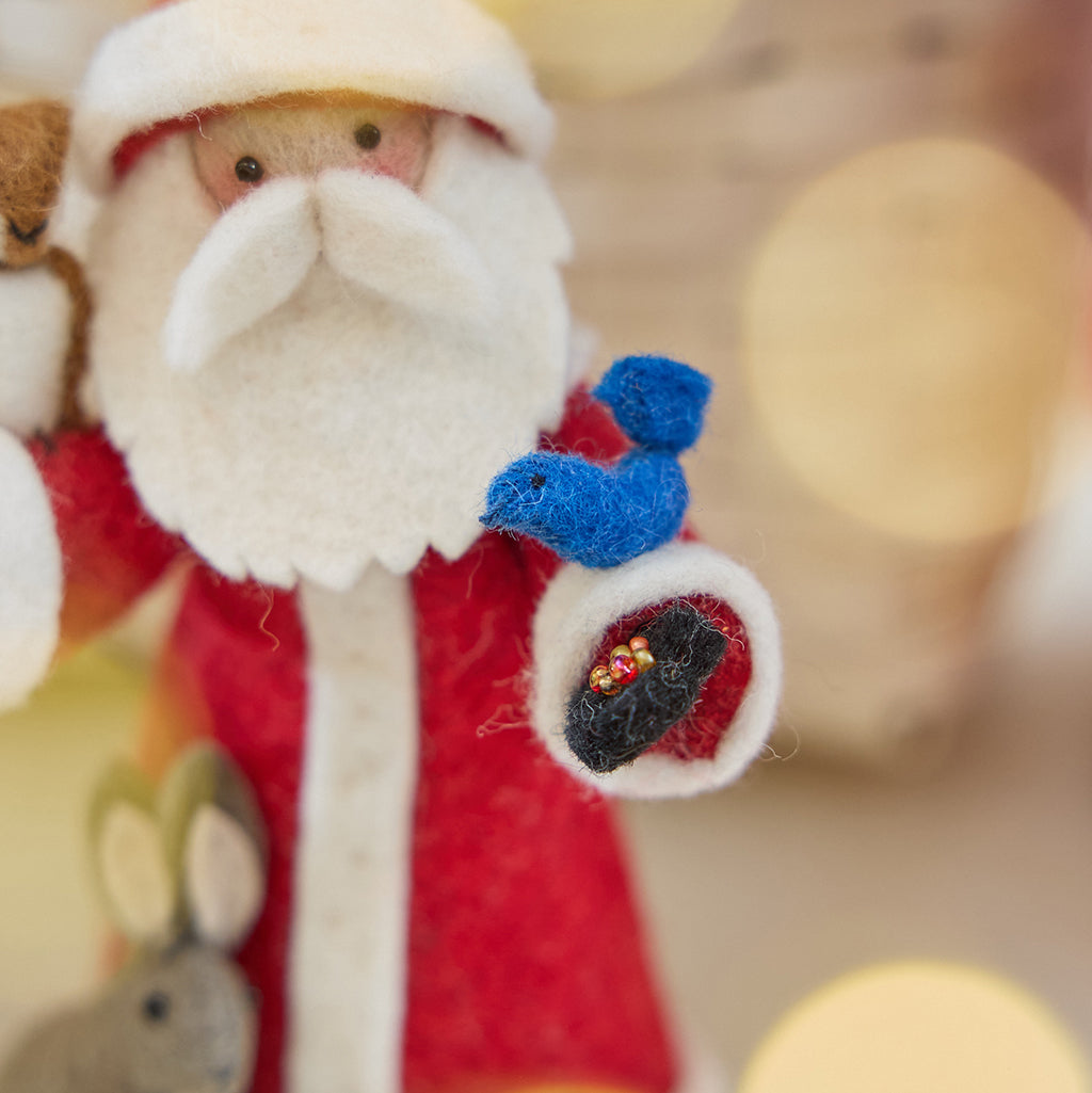Craftspring’s handmade felt Santa with Woodland Animals ornament — close-up detail of the bluebird perched on Santa’s arm, with a hand holding the beaded birdseed, highlighting the intricate felt and beaded details, perfect for Christmas decorating or gifting, ethically crafted by artisans using sustainable wool.