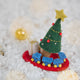 Craftspring’s Train Around the Christmas Tree Ornament — felt blue toy train wrapping around the base of a decorated Christmas tree with presents — displayed on snow with evergreens, capturing cozy holiday magic, whimsical charm, and heirloom-quality Christmas gifting, ethically crafted by artisans using sustainable wool.
