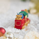 Craftspring’s Toy Train Ornament — felt red and green train with gold embroidery — displayed on snow showing the back with a teddy bear, highlighting whimsical holiday details and heirloom-quality gifting, ethically crafted by artisans using sustainable wool.