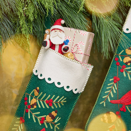 Craftspring’s handmade felt Woodland Stocking ornament — featuring intricate applique and embroidered details, including a cardinal sitting on a pine branch, displayed hanging on a fireplace mantle with evergreens and stuffed with presents for a festive holiday scene, perfect for Christmas decorating or gifting, ethically crafted by artisans using sustainable wool.