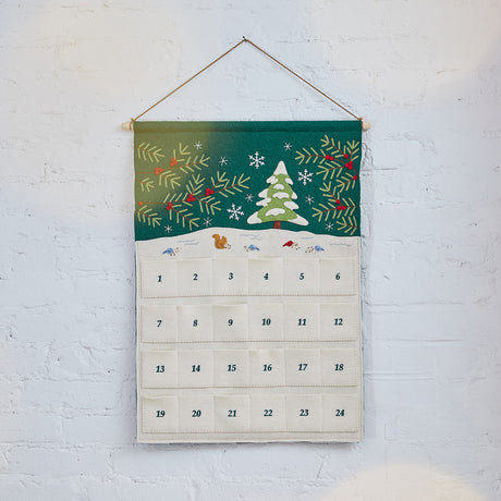 Craftspring’s Woodland Advent Calendar — handmade felt calendar with appliqué, embroidered, and beaded details of a snowy woodland scene featuring a snowy tree, birds, a squirrel, evergreen branches with red berries, and snowflakes — heirloom-quality Christmas decor, ethically crafted by artisans using sustainable wool.