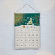 Craftspring’s Woodland Advent Calendar — handmade felt calendar with appliqué, embroidered, and beaded details of a snowy woodland scene featuring a snowy tree, birds, a squirrel, evergreen branches with red berries, and snowflakes — heirloom-quality Christmas decor, ethically crafted by artisans using sustainable wool.