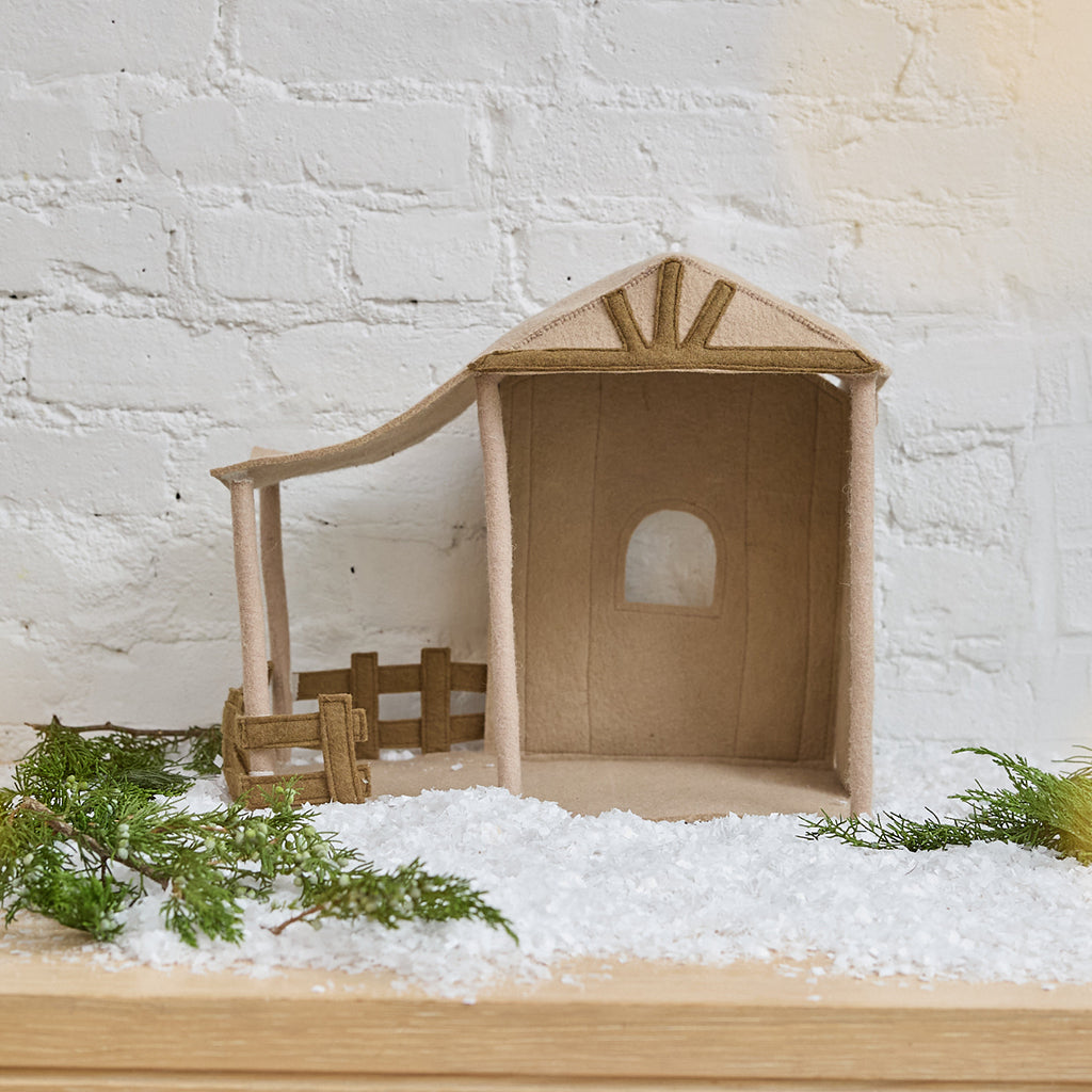 Craftspring’s Nativity Barn displayed on snow with fresh evergreens — handmade felt holiday decor designed to house the Holy Night Nativity Scene, ethically crafted by artisans using sustainable wool.
