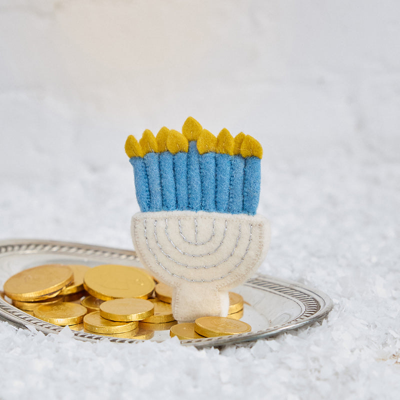 Craftspring’s Small Silver Menorah ornament displayed on snow with gelt — handmade from felt with silver embroidery and blue candles, a festive Hanukkah holiday decoration ethically crafted by artisans using sustainable wool.