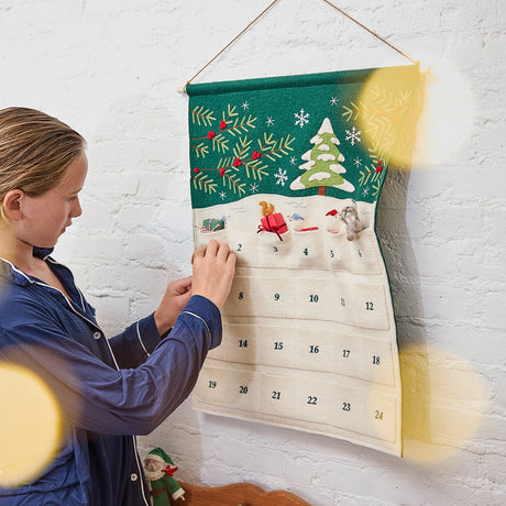 Craftspring’s Woodland Advent Calendar with a girl looking into one of the pockets — the felt calendar features embroidered, appliqué, and beaded woodland details, creating a festive holiday moment full of wonder and gifting joy, ethically crafted by artisans using sustainable wool.