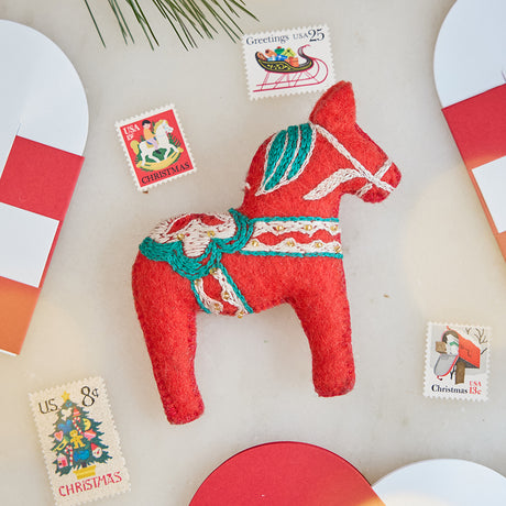 Handmade felt Swedish Dala Horse Ornament from Craftspring, with intricate embroidered and beaded details, displayed among vintage stamps and paper hearts—heirloom-quality Christmas decor, perfect for holiday gifting, ethically handcrafted by artisans using sustainable wool.
