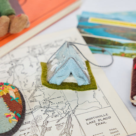 Craftspring’s handmade felt Home Under the Stars Tent ornament — applique and embroidered mountains with the Big Dipper on the side and a mini felt mattress inside the tent, displayed on a trail map for an adventurous holiday scene, perfect for Christmas decorating or gifting, ethically crafted by artisans using sustainable wool.