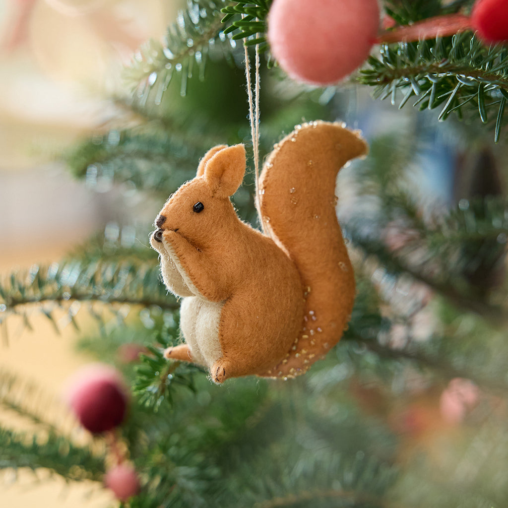 Craftspring’s Red Squirrel ornament — featuring delicate beaded and embroidered details, displayed on a Christmas tree for a festive woodland holiday scene, ethically crafted by artisans using sustainable wool.