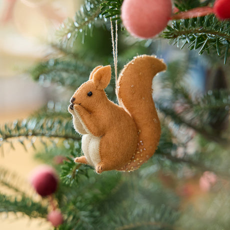 Craftspring’s Red Squirrel ornament — featuring delicate beaded and embroidered details, displayed on a Christmas tree for a festive woodland holiday scene, ethically crafted by artisans using sustainable wool.