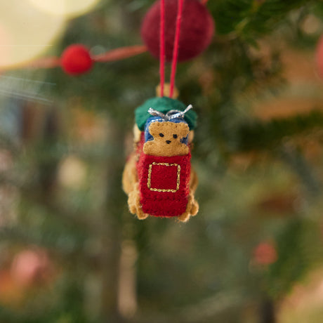 Craftspring’s Toy Train Ornament displayed on a Christmas tree — felt red and green train with gold embroidery, intricately detailed with a team engine carrying presents and a teddy bear, adding festive warmth and whimsical charm — heirloom-quality Christmas decor, ethically crafted by artisans using sustainable wool.