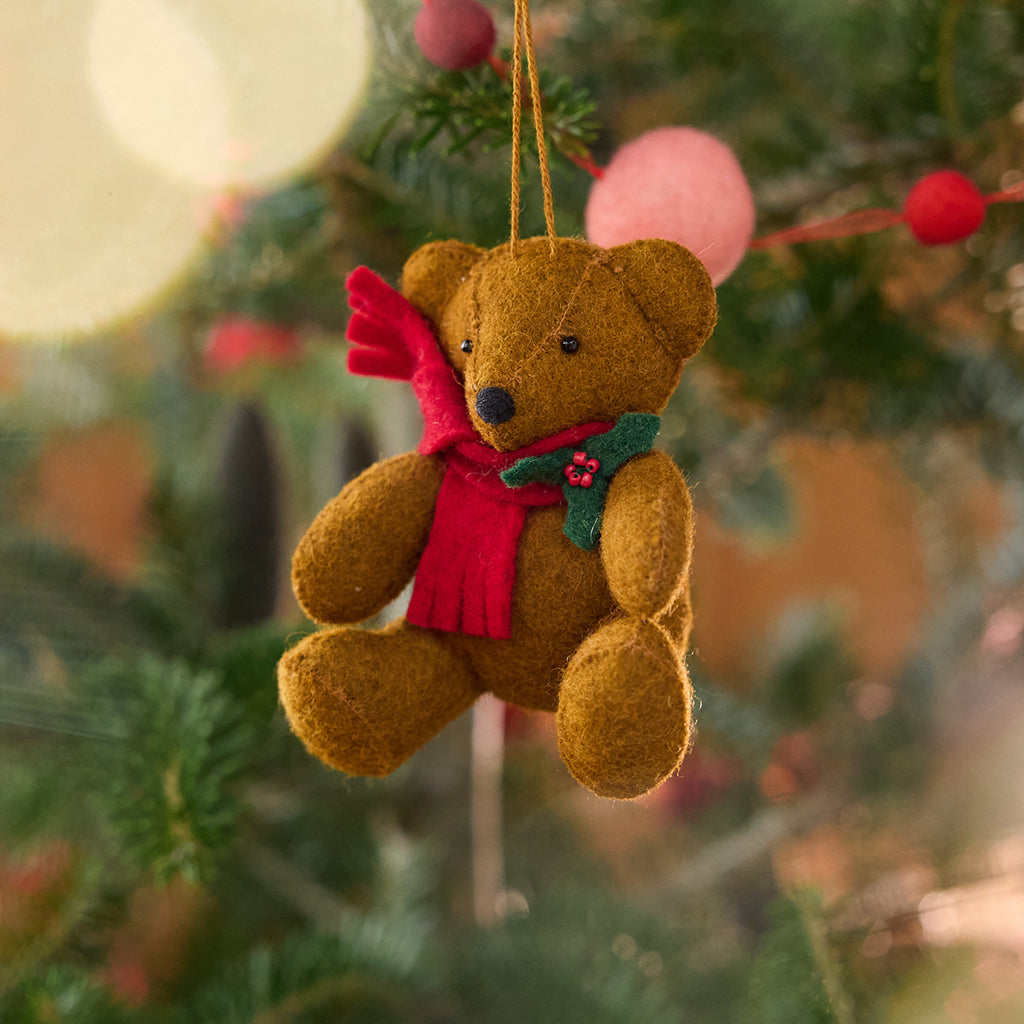 Craftspring’s Holiday Teddy Bear Ornament displayed on a Christmas tree — felt vintage-style teddy bear wearing a red scarf with holly, adding festive warmth and whimsical holiday charm — heirloom-quality Christmas decor, ethically crafted by artisans using sustainable wool.