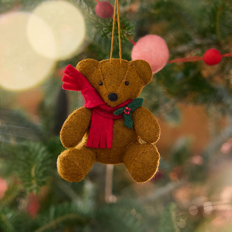 Craftspring’s Holiday Teddy Bear Ornament displayed on a Christmas tree — felt vintage-style teddy bear wearing a red scarf with holly, adding festive warmth and whimsical holiday charm — heirloom-quality Christmas decor, ethically crafted by artisans using sustainable wool.