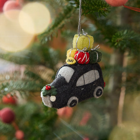 Craftspring’s London Black Cab ornament — featuring intricate beaded and embroidered details, including presents and holly on top of the car, displayed on a Christmas tree for a festive holiday scene, ethically crafted by artisans using sustainable wool.