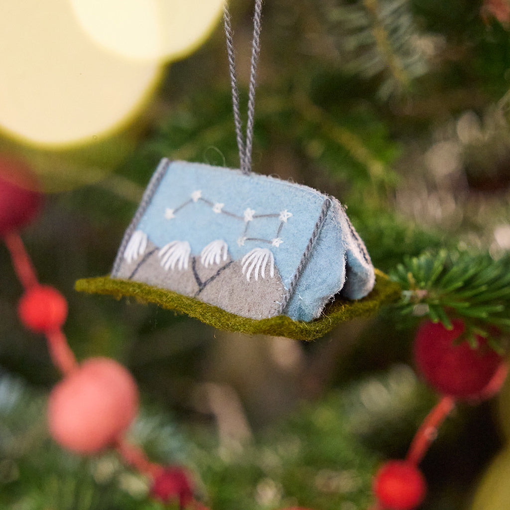 Craftspring’s Home Under the Stars Tent Ornament displayed on a Christmas tree — felt ornament with applique and embroidered mountains, the Big Dipper on the side, and a mini felt mattress inside, adding whimsical and festive holiday charm, ethically crafted by artisans using sustainable wool.