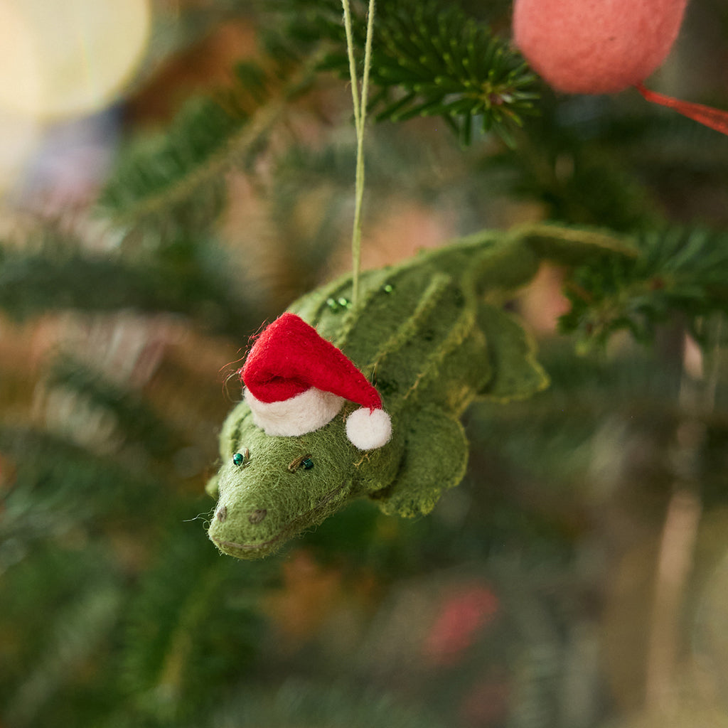 Craftspring’s Santa Alligator Ornament displayed on a Christmas tree — felt alligator with a beautiful face and embroidered and beaded back ridges, adding whimsical holiday charm and festive warmth — heirloom-quality Christmas decor, ethically crafted by artisans using sustainable wool.