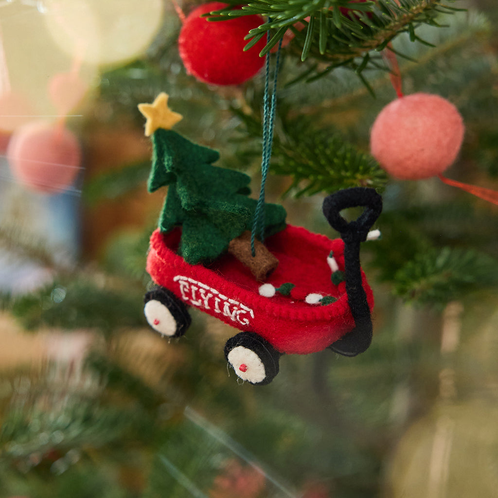 Craftspring’s Little Red Wagon with Tree Ornament displayed on a Christmas tree — felt little red wagon with a Christmas tree and garland inside, featuring embroidered and beaded details, adding festive warmth and whimsical holiday charm — heirloom-quality Christmas decor, ethically crafted by artisans using sustainable wool.