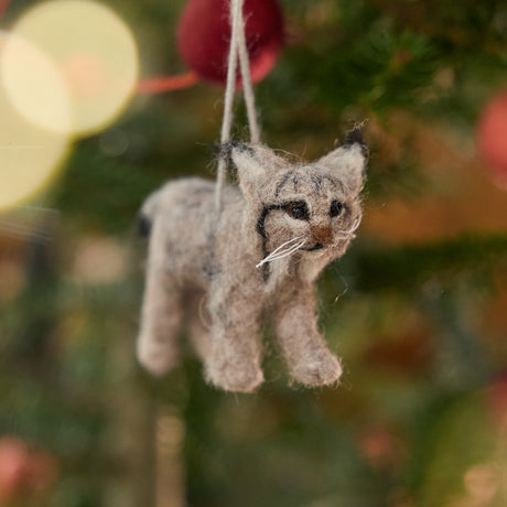 Handmade felt Lynx ornament from Craftspring hanging on a Christmas tree, detailed with realistic whiskers, ear tufts, and a lifelike face — ethically crafted by artisans using sustainable wool for heirloom-quality holiday decorating.