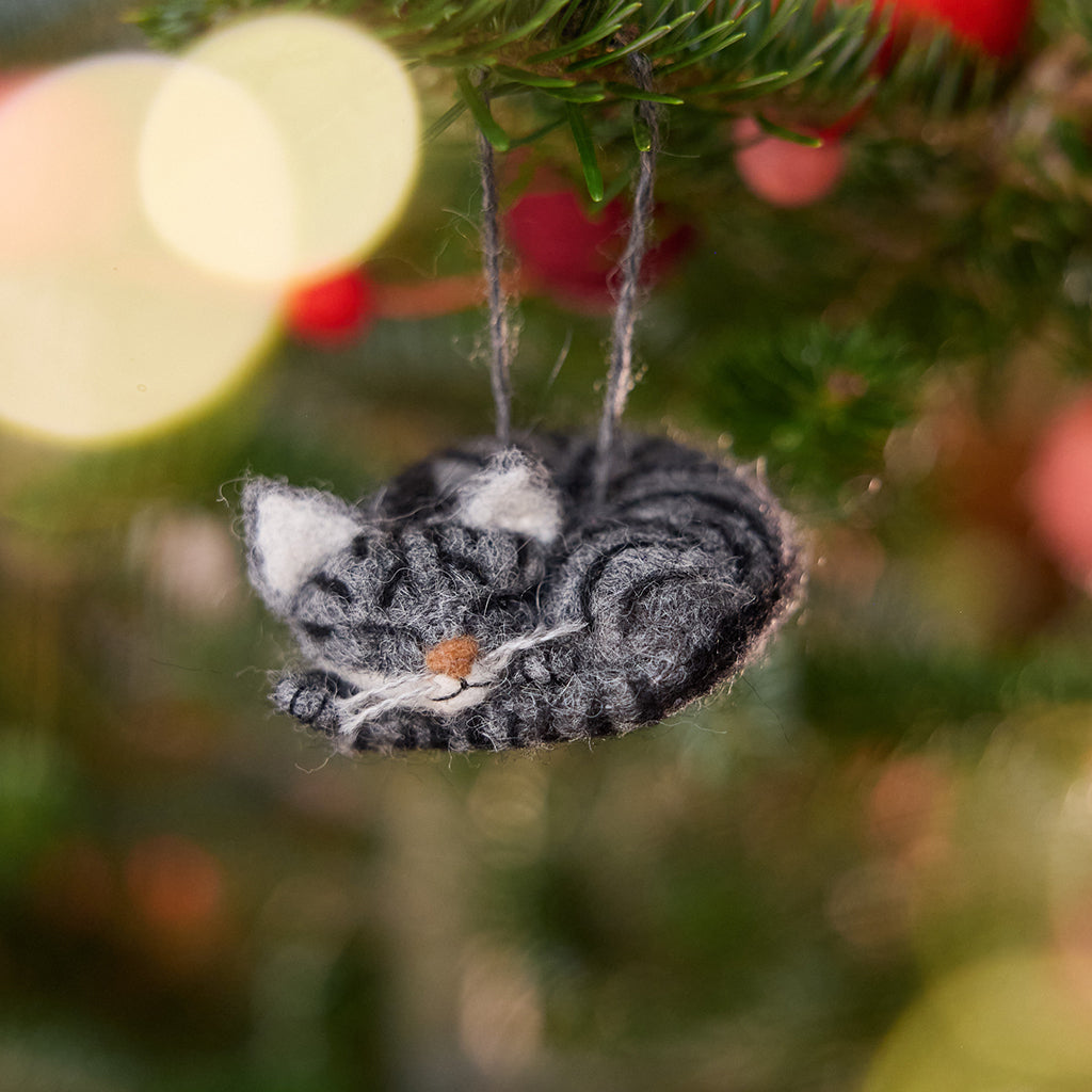 Craftspring’s Sleepy Gray Cat Ornament displayed on a Christmas tree—needle-felted with whiskers and a cute face, adding cozy holiday warmth and gifting charm, ethically crafted by artisans using sustainable wool.
